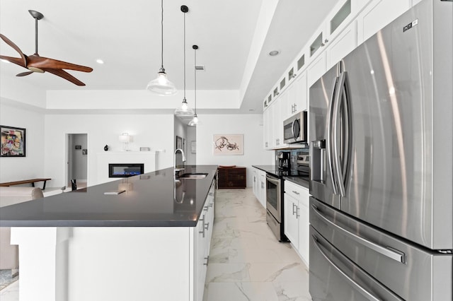 kitchen featuring appliances with stainless steel finishes, white cabinetry, hanging light fixtures, sink, and an island with sink