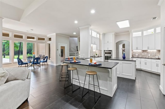 kitchen featuring crown molding, dark countertops, visible vents, a sink, and a kitchen bar