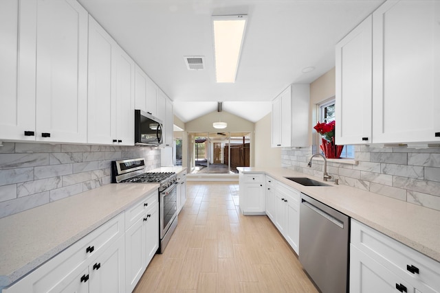 kitchen featuring vaulted ceiling, sink, white cabinets, decorative backsplash, and stainless steel appliances