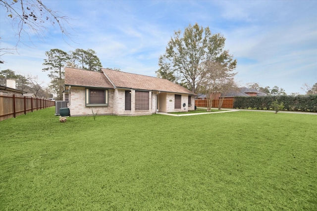 rear view of property with central air condition unit, fence, a lawn, and brick siding