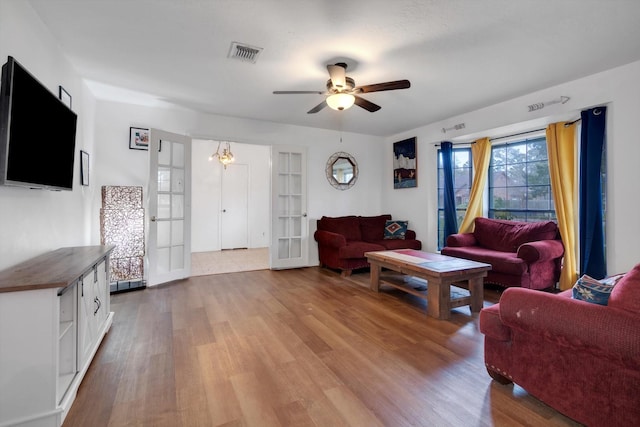 living room featuring light wood-type flooring, ceiling fan with notable chandelier, and french doors