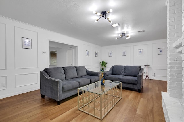 living room featuring light wood-type flooring, visible vents, a decorative wall, and a textured ceiling