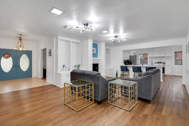 living area with a textured ceiling, light wood-style flooring, a fireplace, visible vents, and an inviting chandelier