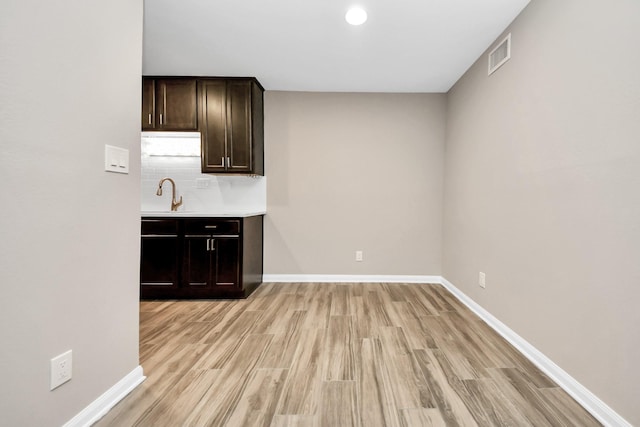 bar featuring dark brown cabinets, light wood-type flooring, decorative backsplash, and sink