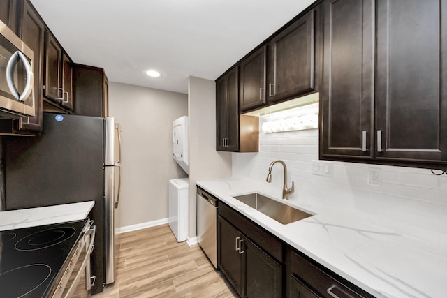 kitchen with light hardwood / wood-style floors, sink, dark brown cabinets, stacked washer / dryer, and stainless steel appliances