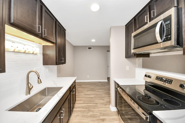 kitchen with light stone countertops, appliances with stainless steel finishes, sink, dark brown cabinetry, and light hardwood / wood-style flooring