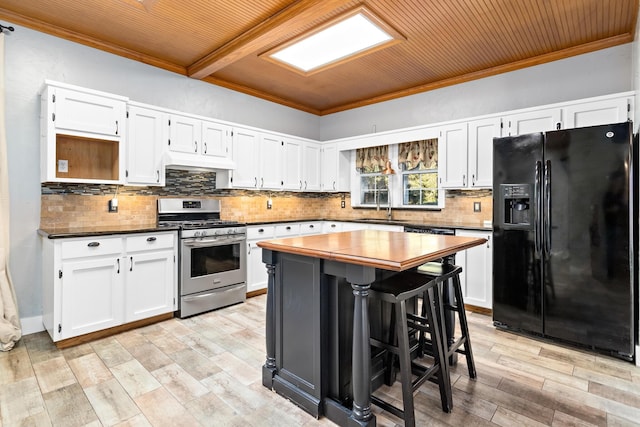 kitchen with light hardwood / wood-style floors, white cabinetry, ornamental molding, black fridge, and stainless steel range with gas cooktop