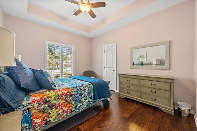 bedroom with ceiling fan, a tray ceiling, and dark hardwood / wood-style flooring