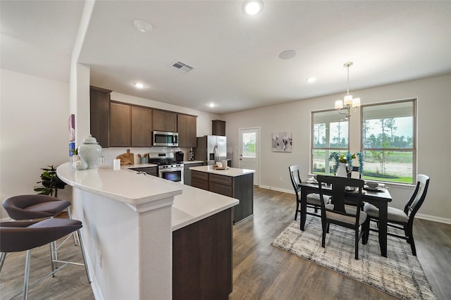 kitchen featuring kitchen peninsula, appliances with stainless steel finishes, decorative light fixtures, dark hardwood / wood-style floors, and a chandelier