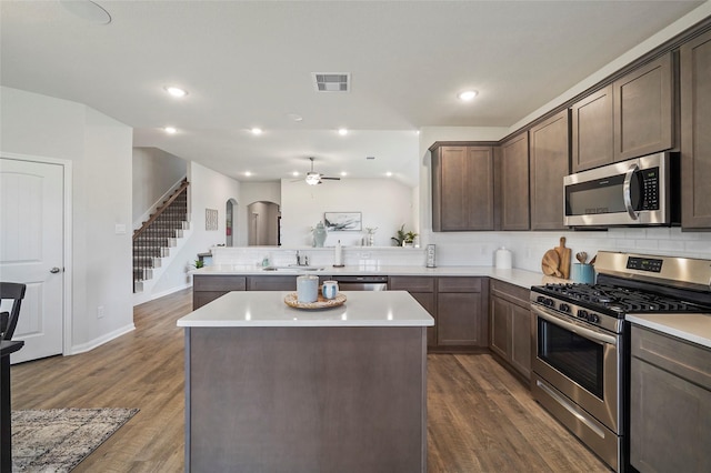 kitchen with appliances with stainless steel finishes, a center island, dark hardwood / wood-style flooring, kitchen peninsula, and dark brown cabinets