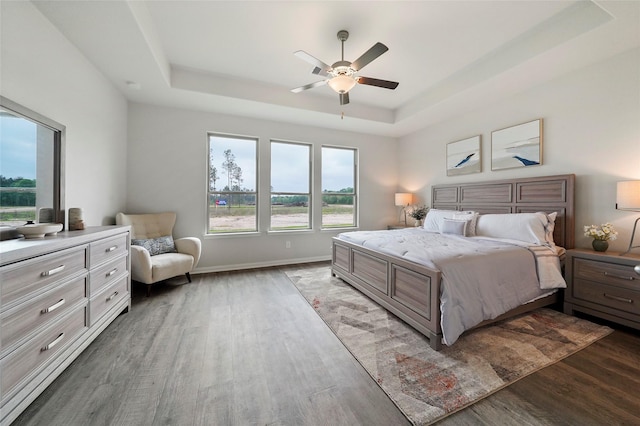 bedroom with dark hardwood / wood-style flooring, ceiling fan, and a raised ceiling