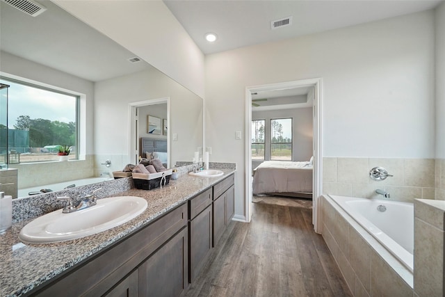 bathroom featuring wood-type flooring, a healthy amount of sunlight, a relaxing tiled tub, and vanity