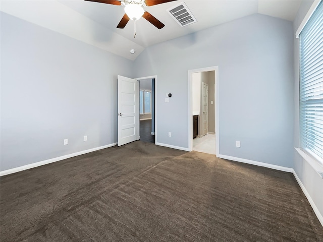 unfurnished bedroom with ceiling fan, dark colored carpet, lofted ceiling, and ensuite bath