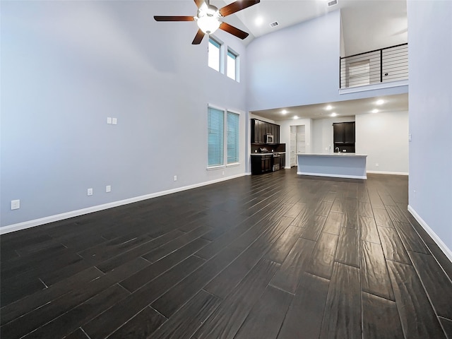 unfurnished living room featuring dark wood-type flooring, a towering ceiling, and ceiling fan