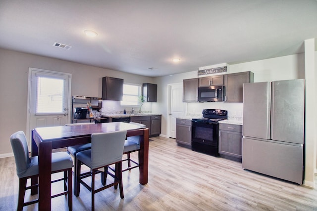 kitchen featuring a wealth of natural light, dark brown cabinetry, black appliances, and light hardwood / wood-style flooring