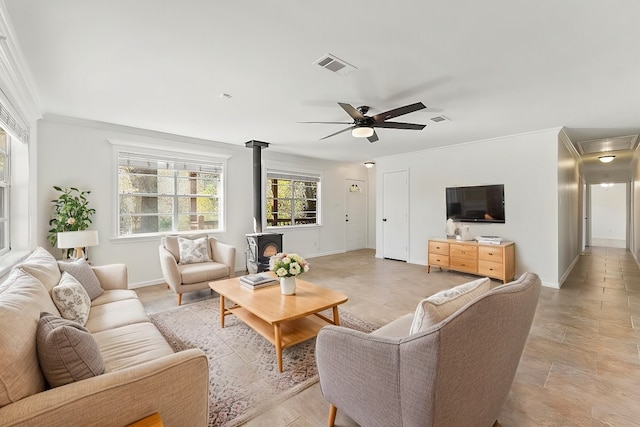 living area with baseboards, visible vents, a ceiling fan, ornamental molding, and a wood stove