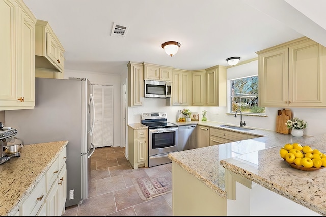 kitchen featuring visible vents, light stone countertops, cream cabinets, stainless steel appliances, and a sink