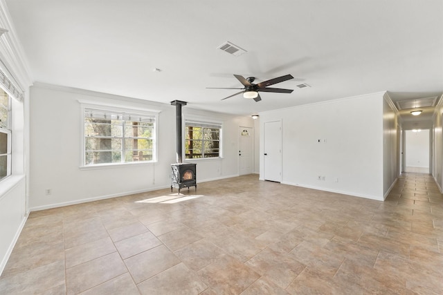 unfurnished living room featuring crown molding, visible vents, a wood stove, ceiling fan, and baseboards