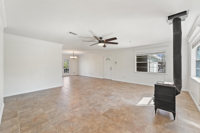 unfurnished living room with crown molding, visible vents, a wood stove, baseboards, and ceiling fan with notable chandelier