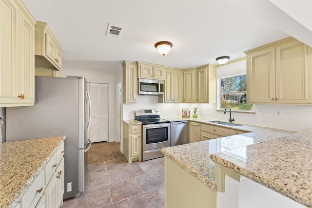 kitchen with visible vents, appliances with stainless steel finishes, light stone counters, cream cabinets, and a sink