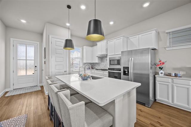 kitchen with pendant lighting, sink, appliances with stainless steel finishes, white cabinets, and a center island with sink