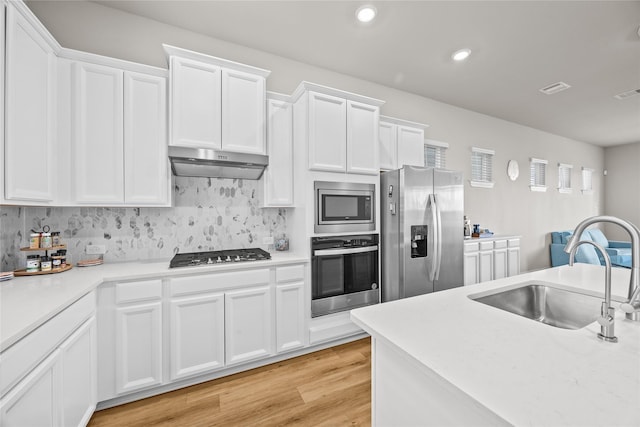 kitchen featuring appliances with stainless steel finishes, tasteful backsplash, sink, white cabinets, and light wood-type flooring