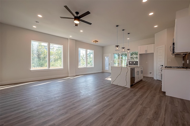 kitchen featuring white cabinets, dark wood-type flooring, stainless steel appliances, hanging light fixtures, and a kitchen island with sink