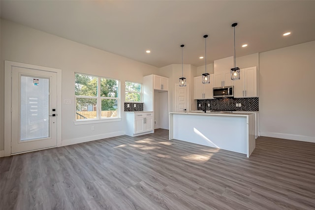 kitchen with white cabinets, a kitchen island with sink, hanging light fixtures, and hardwood / wood-style floors