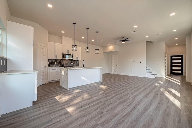 kitchen with white cabinets, light hardwood / wood-style flooring, pendant lighting, an island with sink, and backsplash