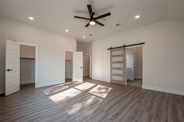 unfurnished bedroom with hardwood / wood-style floors, a closet, ceiling fan, ensuite bathroom, and a barn door