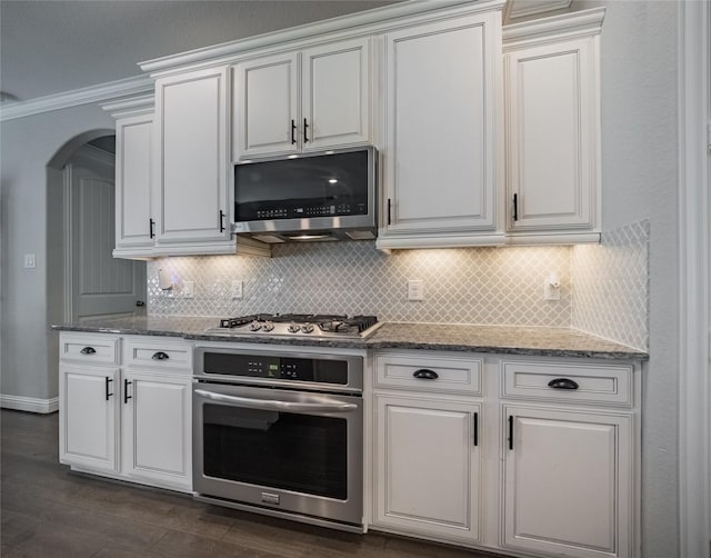 kitchen featuring appliances with stainless steel finishes, backsplash, white cabinets, light stone counters, and crown molding