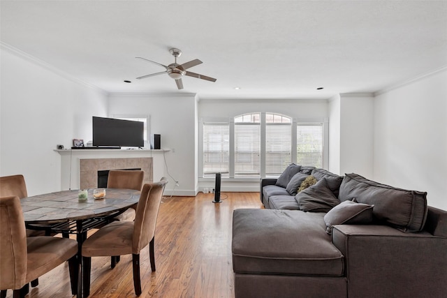 living room featuring light wood-type flooring, ornamental molding, a tiled fireplace, and ceiling fan