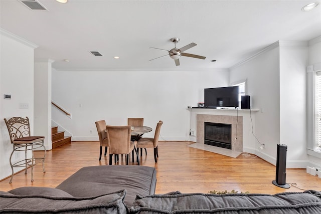 living room featuring light wood-type flooring, a tiled fireplace, crown molding, and ceiling fan