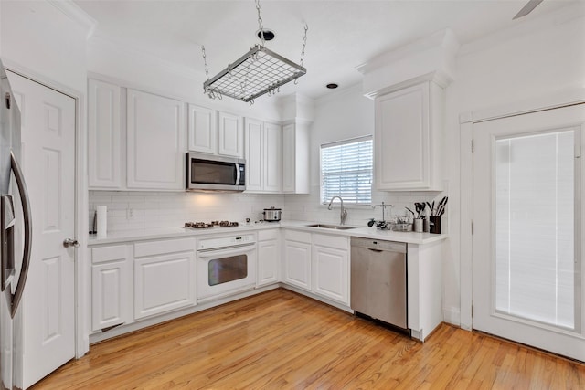 kitchen with light wood-type flooring, white cabinetry, stainless steel appliances, sink, and tasteful backsplash