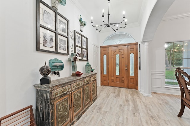 foyer with crown molding, light hardwood / wood-style flooring, a notable chandelier, and ornate columns