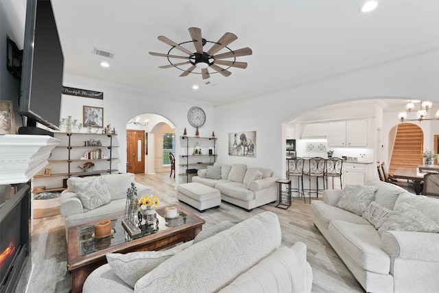 living room with ceiling fan with notable chandelier, ornamental molding, and light hardwood / wood-style floors