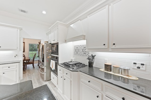 kitchen with white cabinets, appliances with stainless steel finishes, custom exhaust hood, backsplash, and crown molding