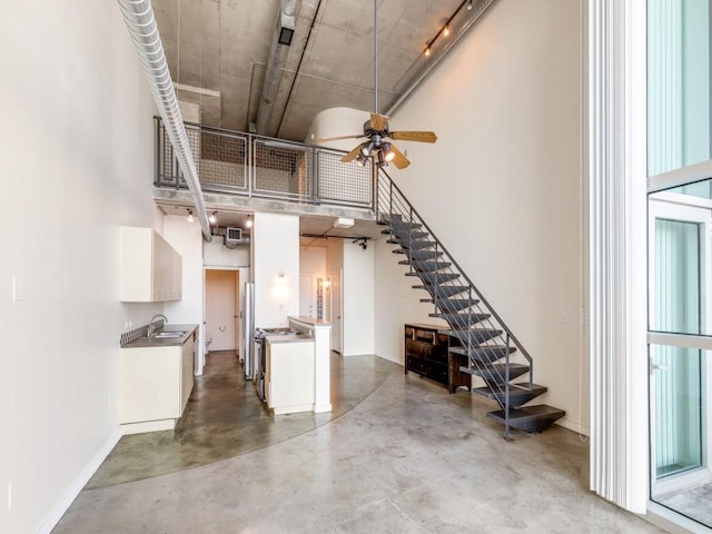 unfurnished living room with concrete floors, sink, ceiling fan, and a towering ceiling