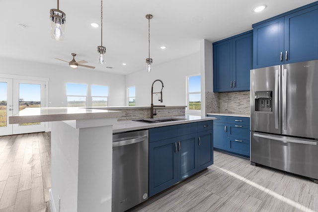 kitchen featuring light countertops, appliances with stainless steel finishes, a sink, an island with sink, and blue cabinets