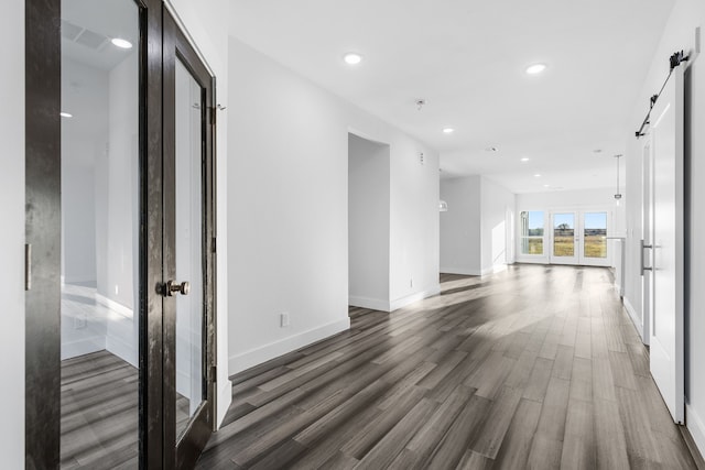 empty room with a barn door, recessed lighting, dark wood-style flooring, baseboards, and french doors