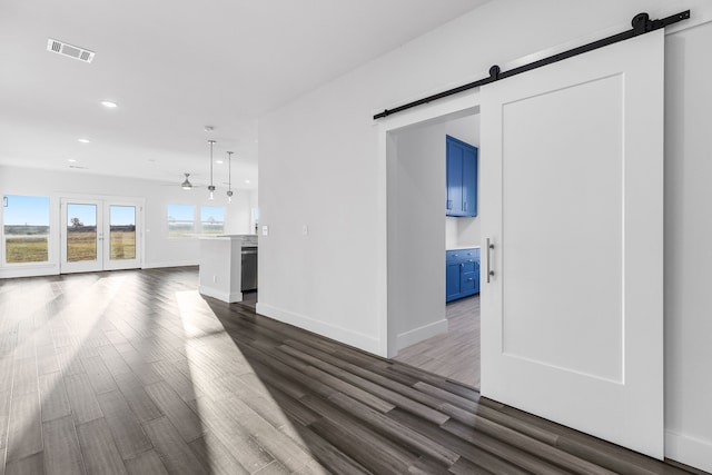 unfurnished living room with a barn door, visible vents, baseboards, dark wood-style floors, and recessed lighting