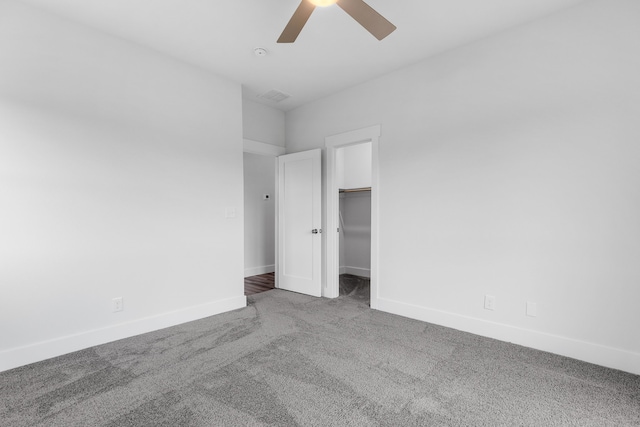 unfurnished bedroom featuring carpet floors, a ceiling fan, visible vents, baseboards, and a walk in closet