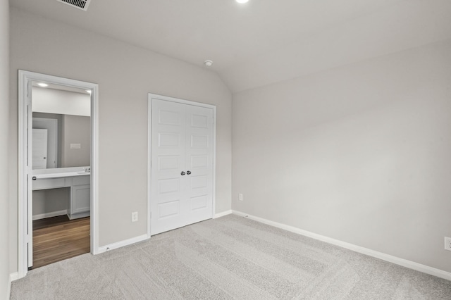 unfurnished bedroom featuring light colored carpet, ensuite bathroom, and vaulted ceiling