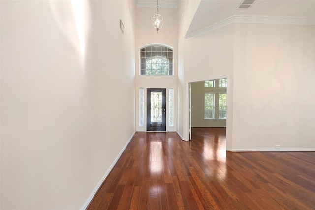 entryway with a notable chandelier, a towering ceiling, crown molding, and dark hardwood / wood-style floors