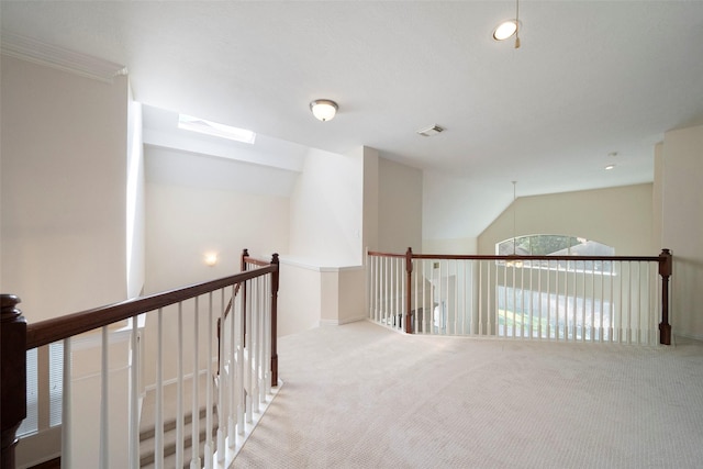 hallway featuring ornamental molding, light carpet, and vaulted ceiling with skylight