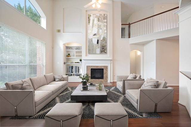 living room featuring built in features, dark wood-type flooring, a tiled fireplace, and a high ceiling