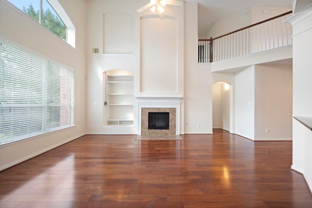 unfurnished living room with built in features, a high ceiling, a tile fireplace, and dark wood-type flooring