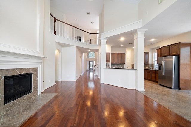 unfurnished living room with a towering ceiling, dark hardwood / wood-style flooring, ornate columns, and a tiled fireplace