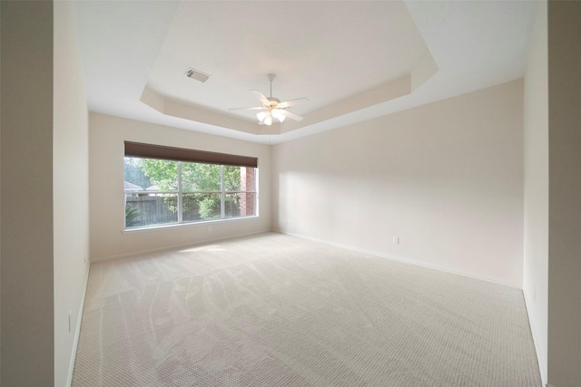 carpeted spare room featuring ceiling fan and a raised ceiling