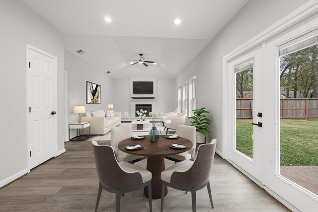 dining space with ceiling fan, wood-type flooring, lofted ceiling, and a fireplace